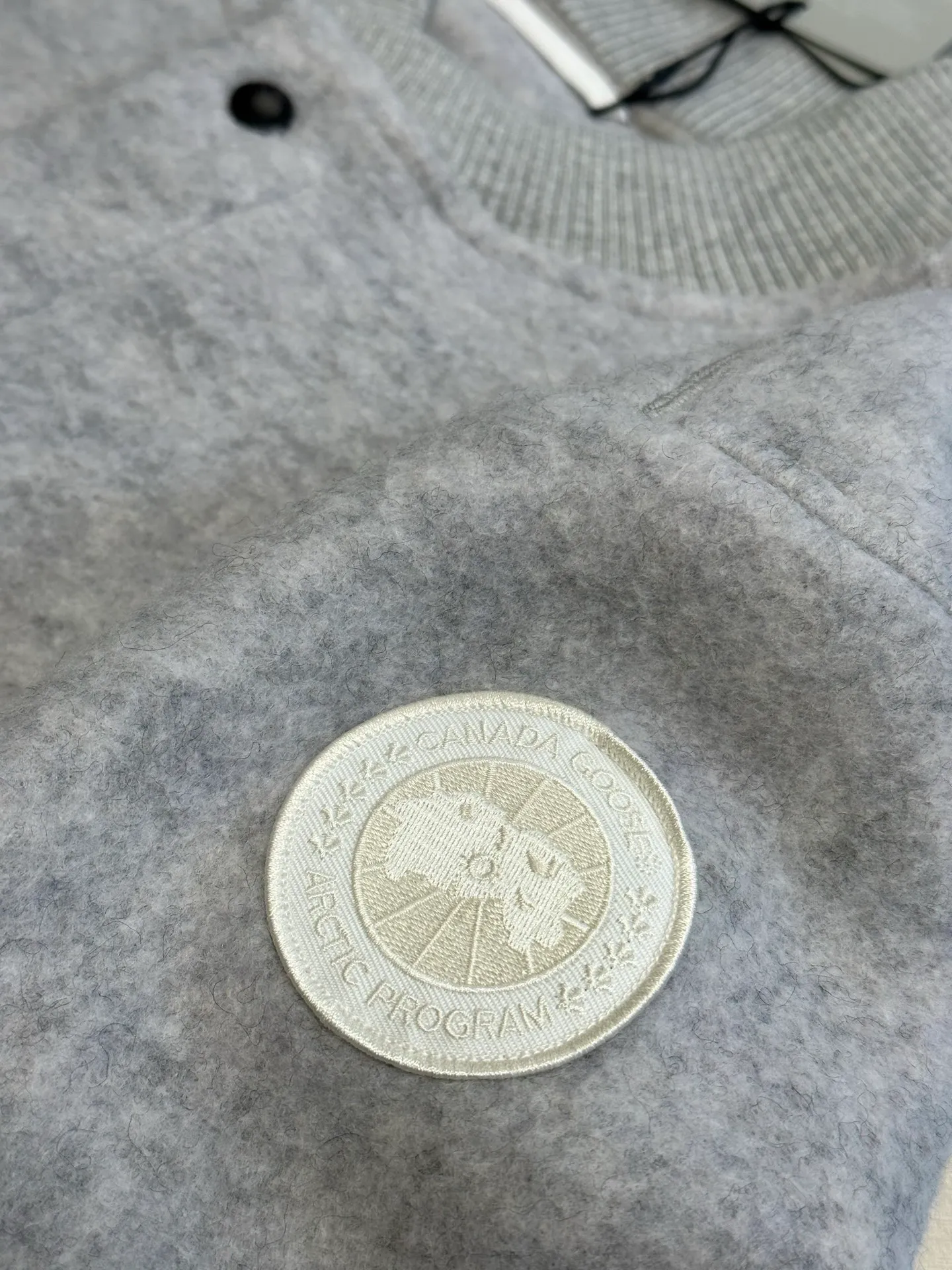 P770 Canada Goose Fleece Badge Button Jacket The main fabric of this jacket is light gray wool blend fabric to improve the fabric's wear resistance, wrinkle resistance and warmth. Wool provides good warmth and a natural feel, while blended fibers enhance the fabric's practicality and durability.  The cutting process needs to ensure that the texture and color of the fabric are evenly distributed, especially with this light gray tone, to avoid chromatic aberrations. The stretchability of wool-blend fabrics needs to be taken into consideration when cutting pieces to ensure dimensional stability of the finished garment.  Use a sewing needle and thread suitable for wool-blend fabrics to avoid damage to the fabric during sewing. The sewing stitches are even and firm to prevent thread stripping.  The temperature needs to be controlled during ironing to avoid high temperature damage to the fabric while keeping the fabric smooth and crisp. The front and back body parts, sleeves and other main parts are stitched with flat seams to ensure a smooth silhouette. Align the fabric texture at the splices to keep the look neat.  The white circular armband on the left arm is an important part of the brand identity and is finely sewn to ensure it is strong and flat.  size：s m l xl